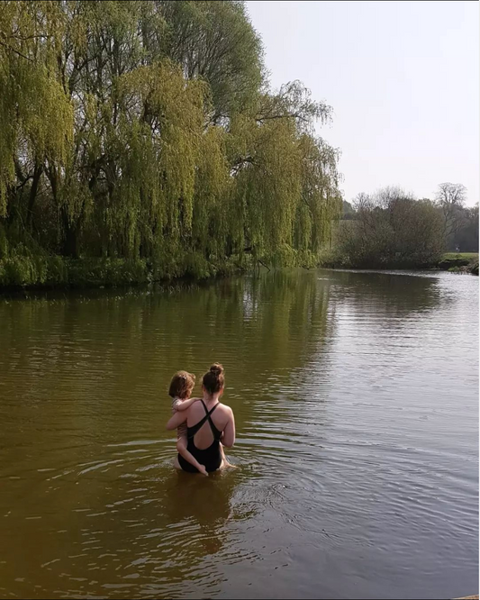 Agnes holding her child while standing in the River Ouse. A willow tree is on the left hand side.