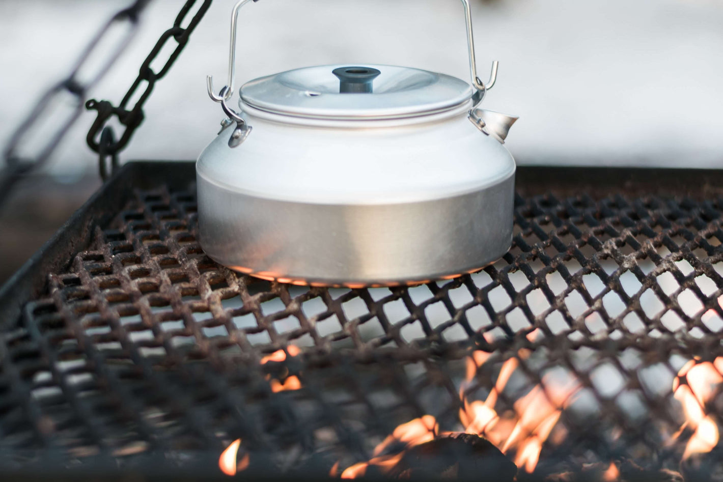 White kettle hanging over a campfire with a blurred natural background